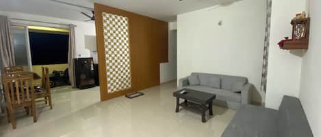 A living room with a sofa, a coffee table, a TV, a ceiling fan, and a sliding door leading to a balcony.