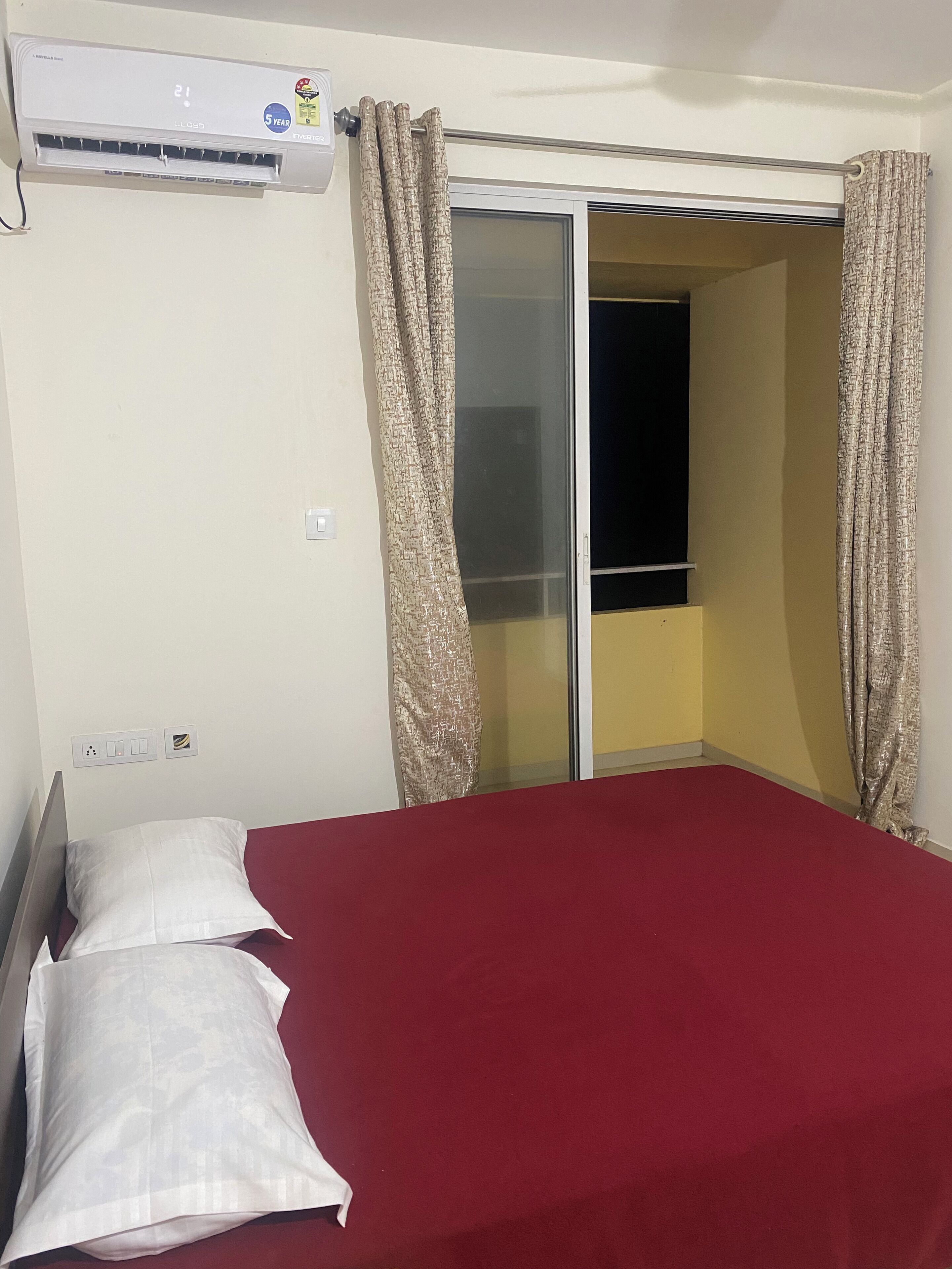 A room with a bed, an air conditioning unit, a sliding door, and a window.