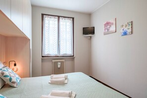 Quarto com cama, janela com cortinas, televisão e duas obras de arte penduradas na parede.
