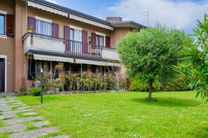 Une maison à deux étages avec un balcon, un jardin avec un arbre et un chemin en pierre.