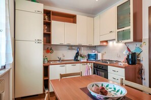 A compact kitchen with white cabinets, a wooden countertop, a stove, a microwave, and a sink.