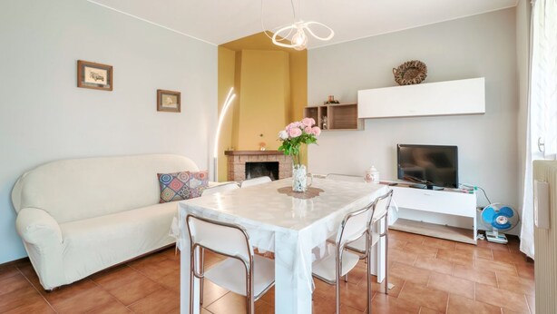 Ein modernes Wohnzimmer mit einem weißen Sofa, einem Esstisch mit Stühlen, einem Kamin, einem Fernseher und einem Ventilator.