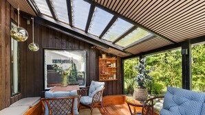 A cozy interior with a wooden floor, a large window, and a seating area with patterned cushions and wicker chairs. - Beautiful Holiday Home in Blokhus (Blokhus)