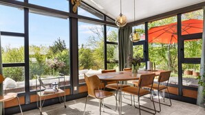A dining area with a large table and chairs, large windows, and an outdoor view. - Beautiful Holiday Home in Blokhus (Blokhus)