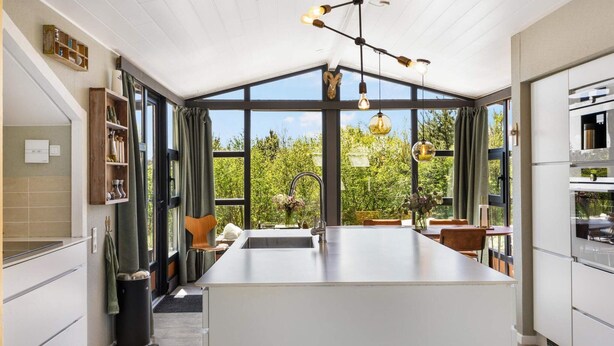 A modern kitchen with a central island, large windows, and a hanging light fixture. - Beautiful Holiday Home in Blokhus (Blokhus)