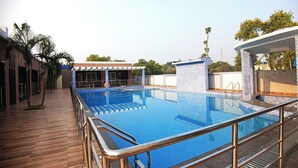 A swimming pool with a wooden deck and a covered seating area. - Sagar Kuthi (Kanthi)