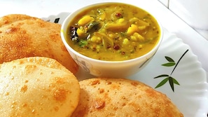 A plate with two golden-brown pancakes and a bowl of yellow curry with vegetables. - Sagar Kuthi (Kanthi)
