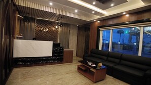 A modern living room with a marble floor, a black sofa, a coffee table, and a reception desk with a herringbone patterned wall. - Sagar Kuthi (Kanthi)