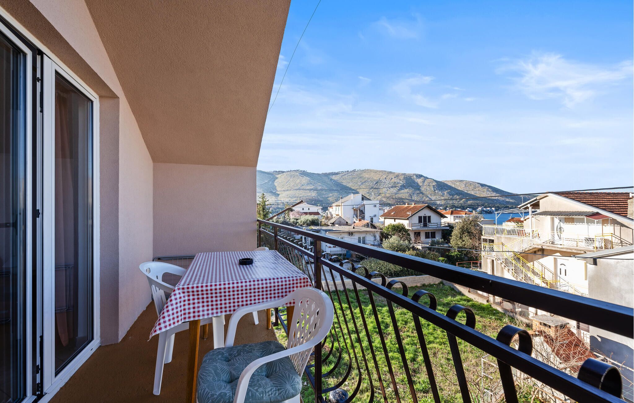 A balcony with a table and chairs, overlooking a residential area and hills.