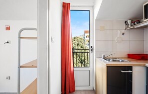 Een compacte keuken met een spoelbak, een klein aanrecht en uitzicht op een balkon met een rood gordijn.