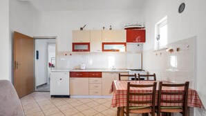 Een compacte keuken met een eethoek, voorzien van een betegelde vloer, een koelkast, een fornuis en een tafel met stoelen.