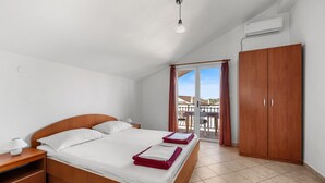 Een slaapkamer met een houten bed, een nachtkastje, een garderobe en een balkon met een tafel en stoelen.