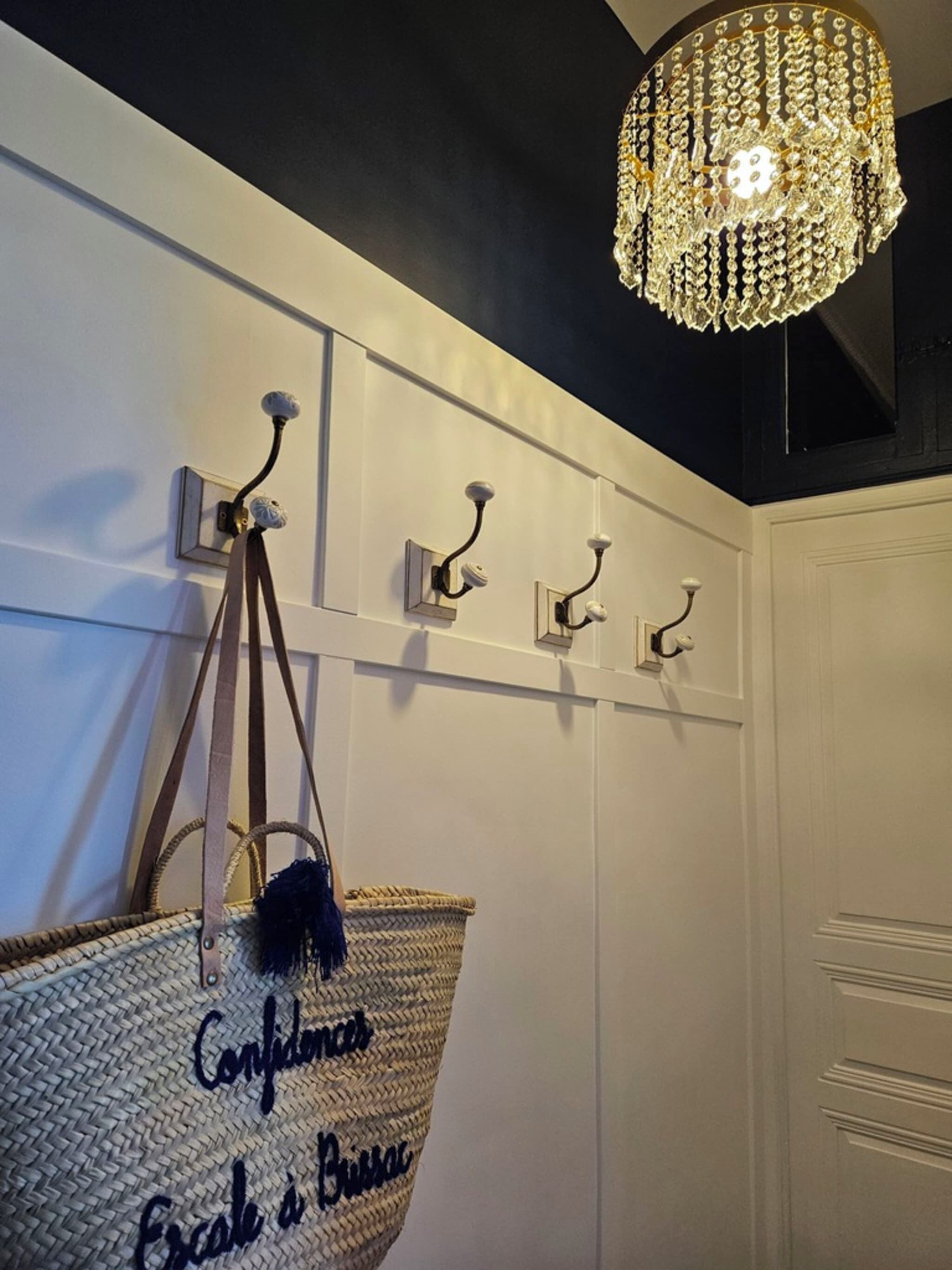 A room with a chandelier, wall-mounted hooks, and a woven bag with text.