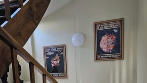 Een houten trap met een leuning, leidend naar een plateau met twee ingelijste posters aan de muur.