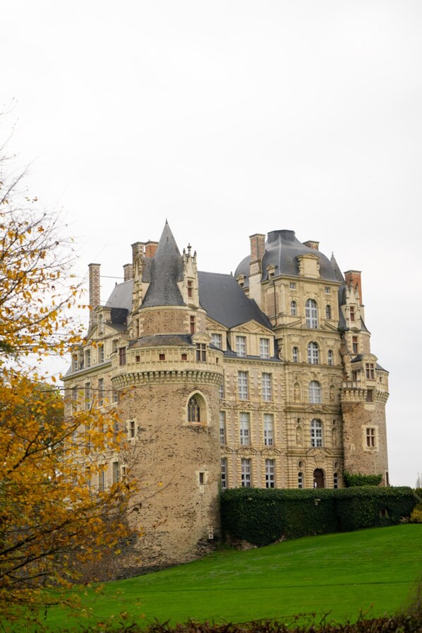 Un edificio grande e histórico con múltiples torres y almenas, rodeado por un césped bien cuidado.