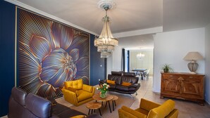 Een moderne woonkamer met een groot abstract schilderij, leren banken, een kroonluchter en een houten kast.
