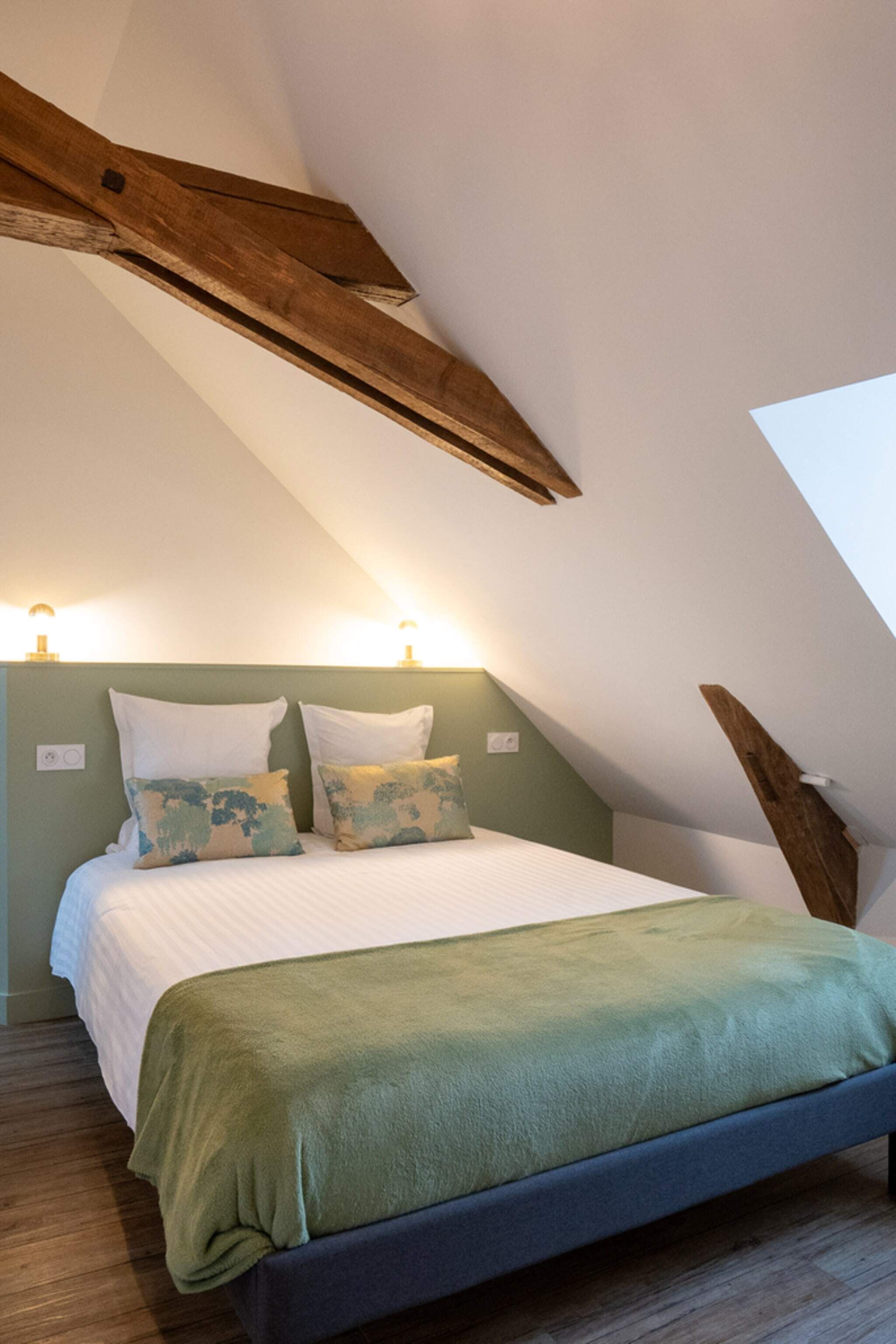 Ein Schlafzimmer mit schrägen Wänden, einem Bett mit grüner Decke und zwei Wandleuchten.