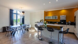 Een moderne keuken met een centraal eiland, barkrukken en een eethoek met tafel en stoelen.