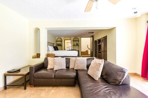 A living room with a brown leather sofa, a small table, and a bed in the background.