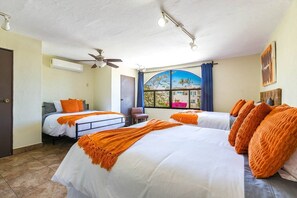 A hotel room with two beds, a ceiling fan, a window with a view, and a door.