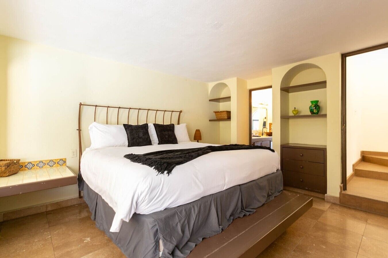 A neatly made bed with a headboard, a bedside table with a lamp, and a bench at the foot of the bed.