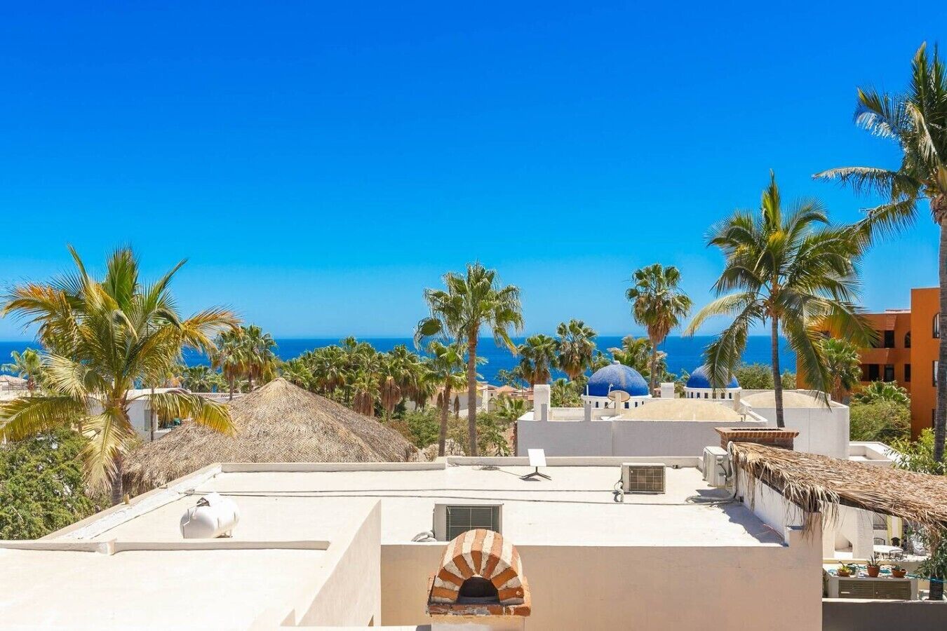 A coastal hotel with a rooftop terrace, palm trees, and a view of the sea.