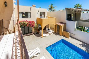 A rooftop pool area with a clear blue pool, white lounge chairs, and a small covered seating area.