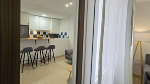Une cuisine moderne avec des meubles blancs, un îlot central doté de tabourets de bar et un canapé gris.
