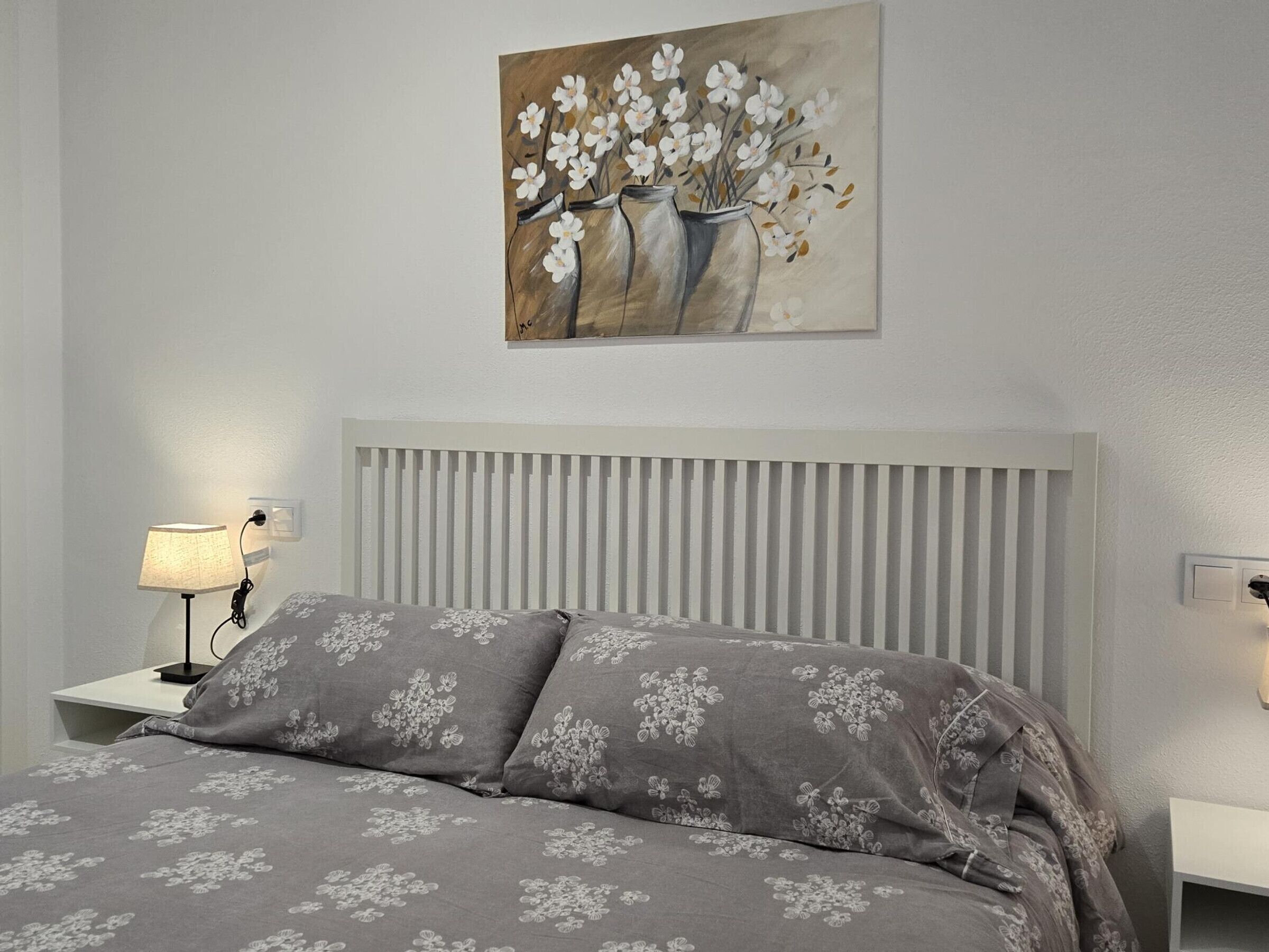 Una camera da letto con un letto, un comodino, una lampada e un quadro appeso.
