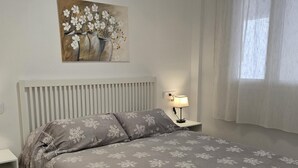 Une chambre à coucher avec un lit, une table de chevet, une lampe, un tableau et une fenêtre avec des rideaux.