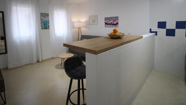 Une cuisine moderne avec un plan de travail en bois, un saladier rempli de fruits et un tabouret de bar.