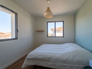 A bedroom with a large bed, a window, and a hanging light fixture. - New house near ocean, terrace, parking, 8 people (Biscarrosse Plage)