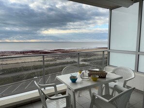 Ein Balkon mit Tisch und Stühlen mit Blick auf Strand und Meer.