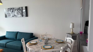 Un coin repas avec une table dressée pour quatre personnes, des chaises blanches et un canapé de couleur turquoise.