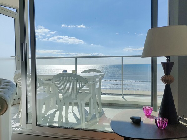Ein Balkon mit Blick auf das Meer, weiße Plastikstühle, ein kleiner Tisch mit rosa Gläsern und eine Lampe.