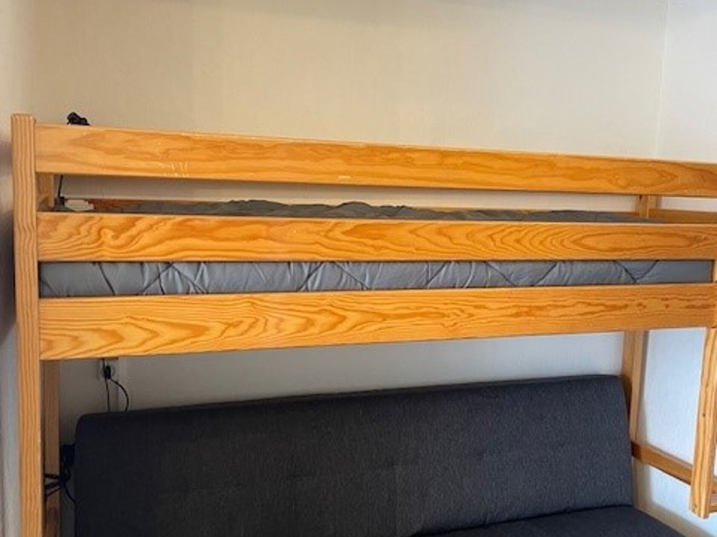 Un lit superposé avec une structure en bois et une tête de lit rembourrée de couleur grise.