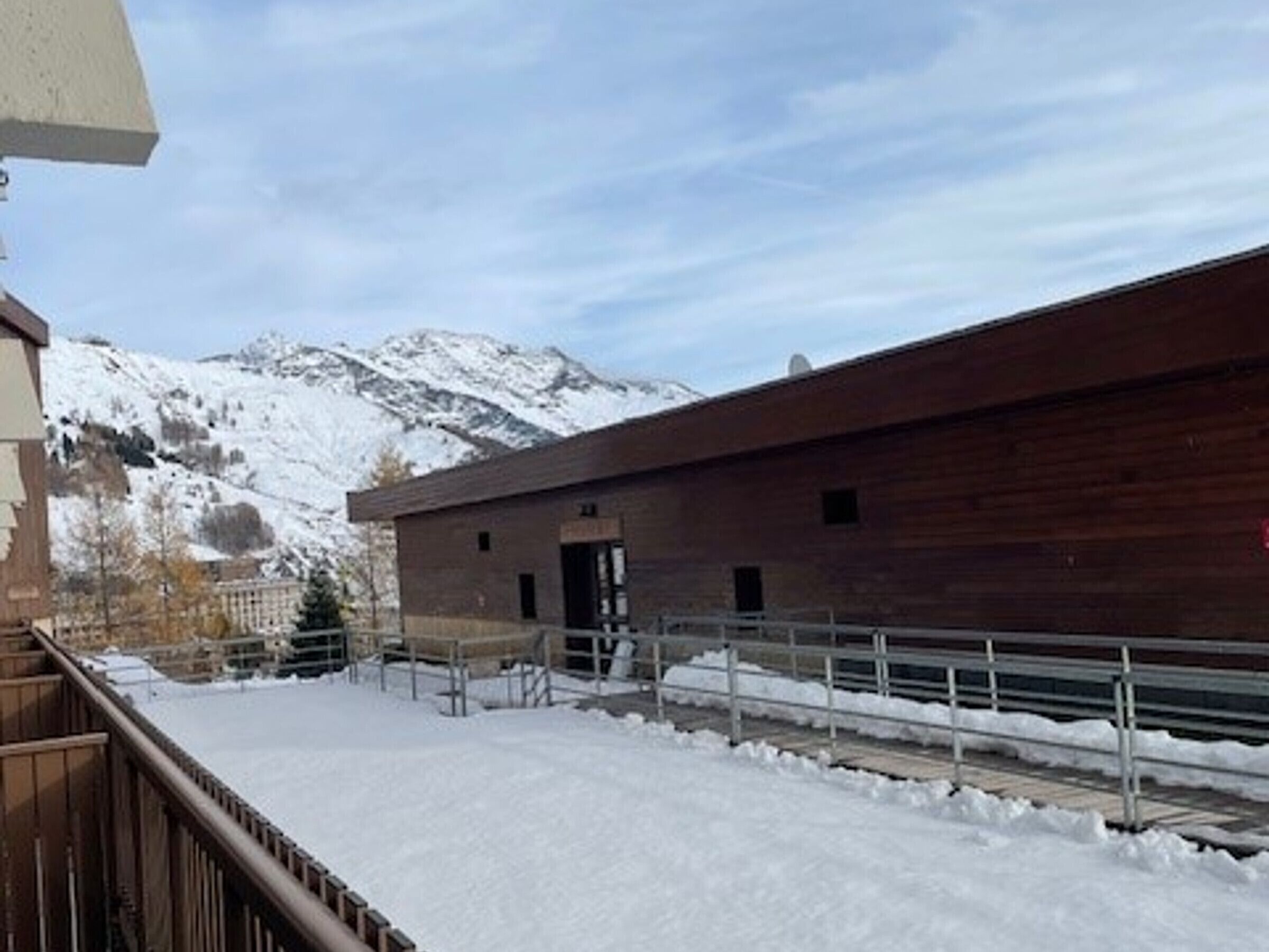 Een modern gebouw met een houten gevel, een metalen hekwerk en een besneeuwde berg op de achtergrond.