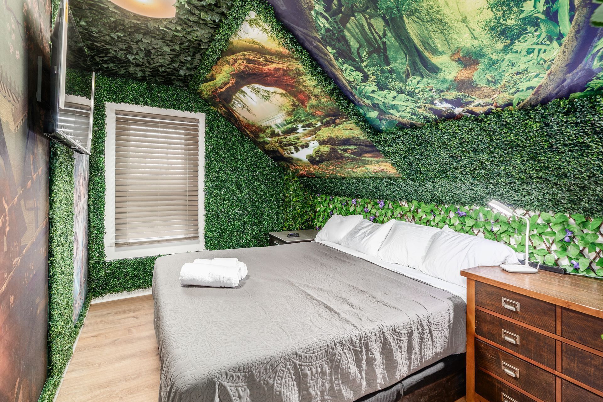 A bedroom with a bed, a wooden dresser, and a wall mural of a forest scene.