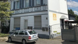 Un edificio de dos pisos con garaje, un coche estacionado en la entrada y un acceso con portón.