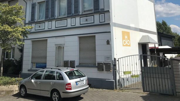 Un edificio de dos pisos con garaje, un coche estacionado en la entrada y un acceso con portón.