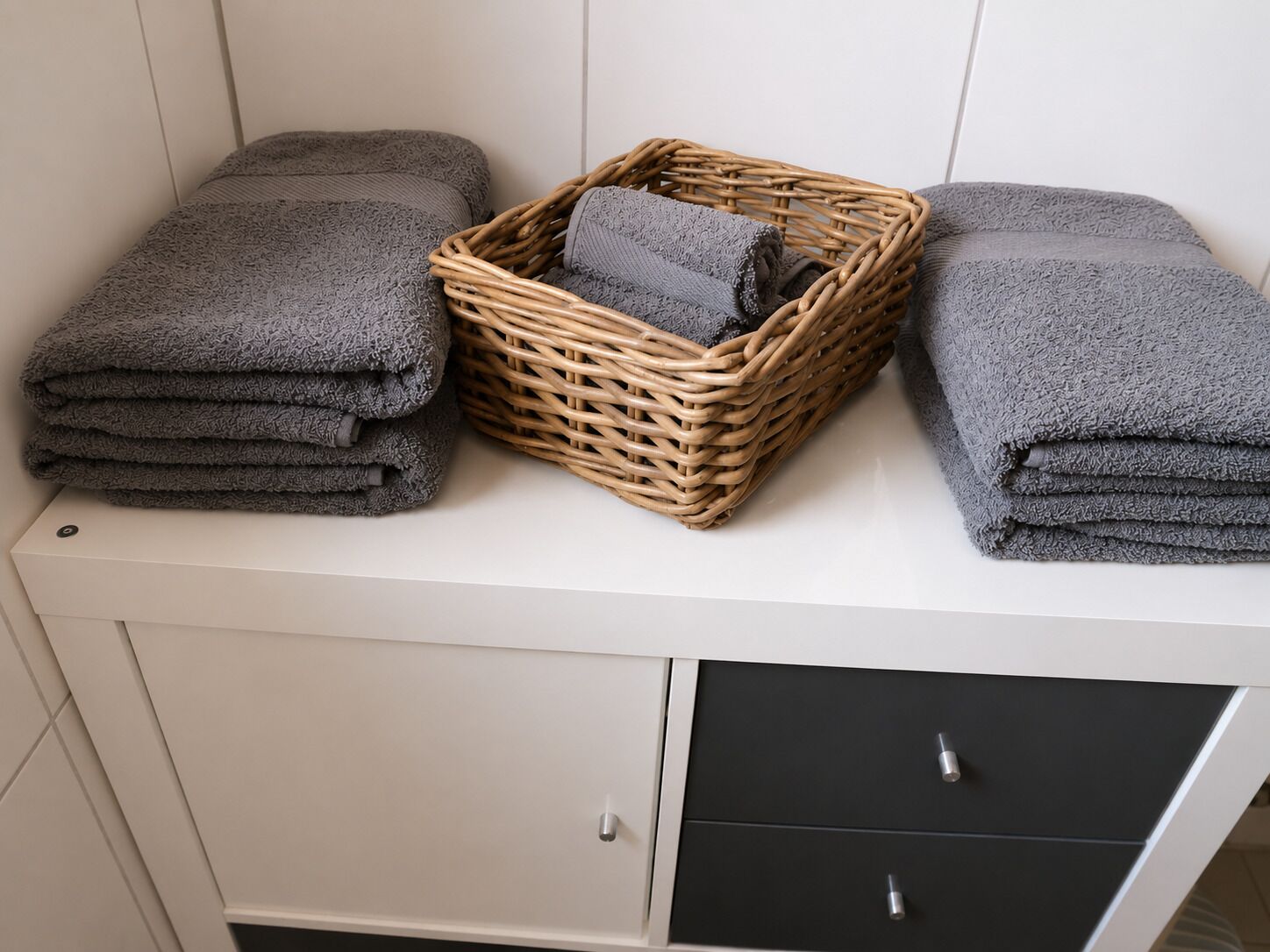 Une salle de bain avec un meuble blanc, deux serviettes et un panier en osier.