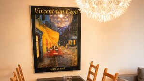 Ein Essbereich mit einem Tisch für vier Personen, einer Kerze und einem Poster von Vincent van Goghs 'Café de nuit' an der Wand.