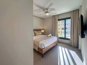 Hotellihuone, jossa on sänky, kattotuuletin, ikkuna verhoilla ja näkymä ulkona oleviin rakennuksiin.