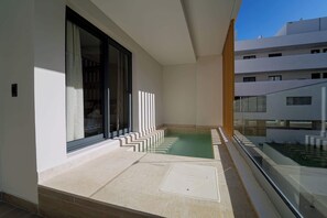 A balcony with a small pool, a glass railing, and a view of adjacent buildings.