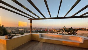 Una terraza en la azotea con vistas a un paisaje urbano, que incluye una pérgola y un pequeño espacio de estar.