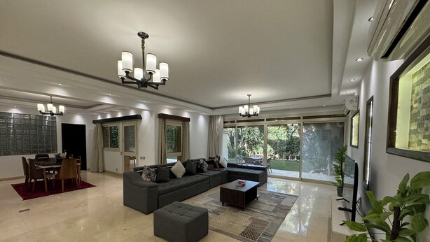 Una sala de estar amplia con un sofá seccional, una zona de comedor y grandes ventanales que ofrecen vistas al exterior.