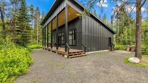 Moderni mökki, jossa on puinen terassi ja suuret ikkunat, ja sen ympärillä on tiheää metsää.
