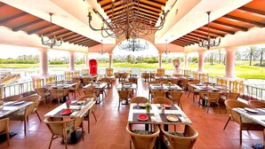 A spacious outdoor restaurant with multiple tables and chairs, a central chandelier, and a view of a landscaped area. - Bright & modern 2 bedroom apartment - TR721LT (La Torre Golf Resort)