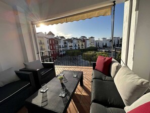 Un balcon aménagé avec du mobilier d’extérieur, une vue sur les bâtiments et un ciel dégagé.