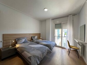 Une chambre avec deux lits, une table de chevet, une chaise et une fenêtre avec des rideaux.